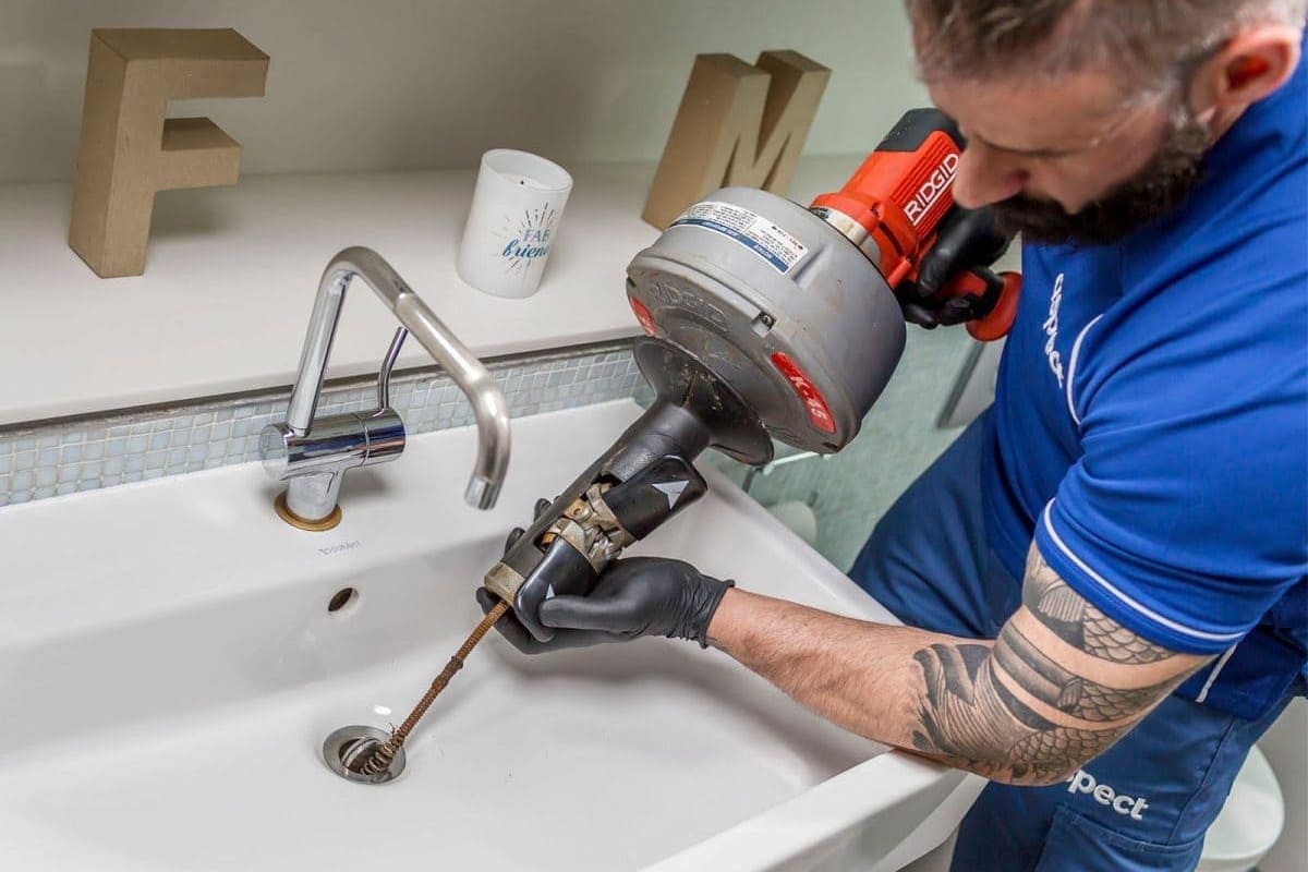 Técnico de desentupidora inspecionando ralo com equipamento profissional