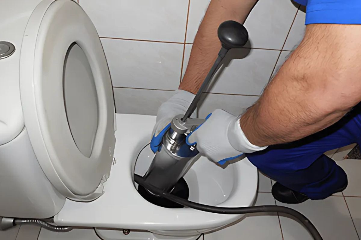 Técnico de desentupidora realizando desentupimento de vaso sanitário com equipamento