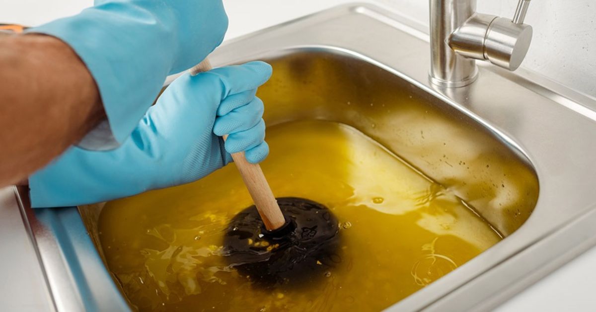 Pessoa tentando desentupir a pia da cozinha com desentupidor de borracha