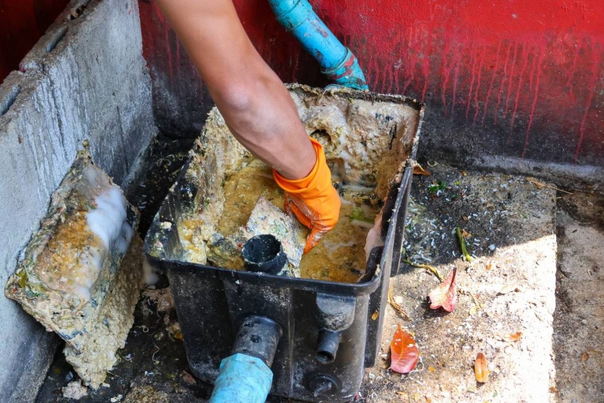 Técnico abrindo encanamento com sinal visível de obstrução por gordura