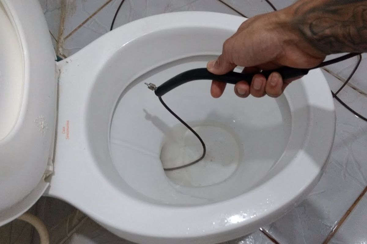 Pessoa utilizando uma sonda desentupidora para desobstruir um vaso sanitário, mostrando a ferramenta sendo inserida no encanamento.