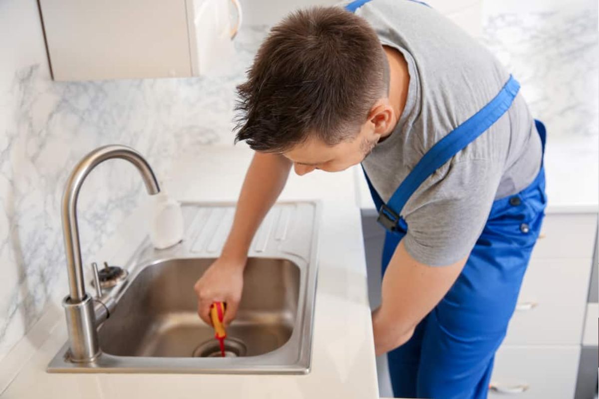 Técnico usando cabo manual para desentupir pia residencial
