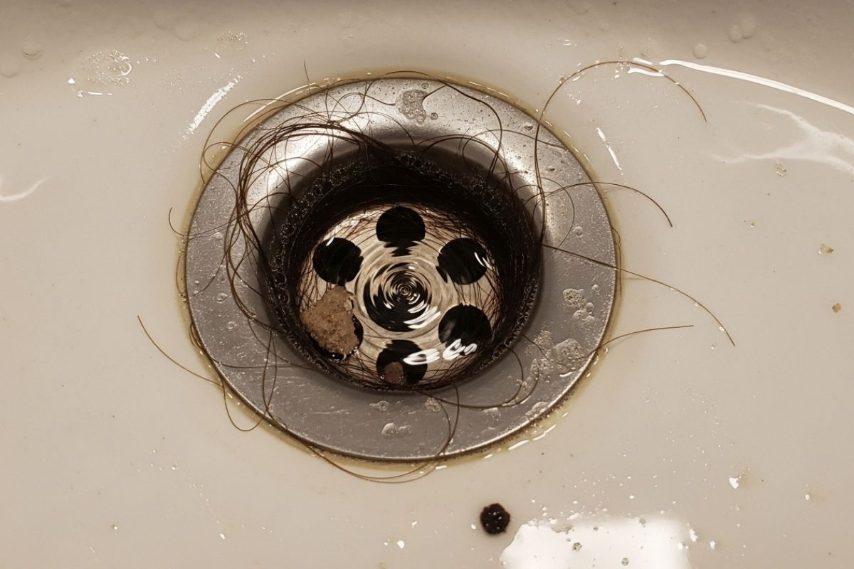 Close em ralo de banheiro com escoamento lento e acúmulo de resíduos, sinal clássico de necessidade de limpeza de fossa.